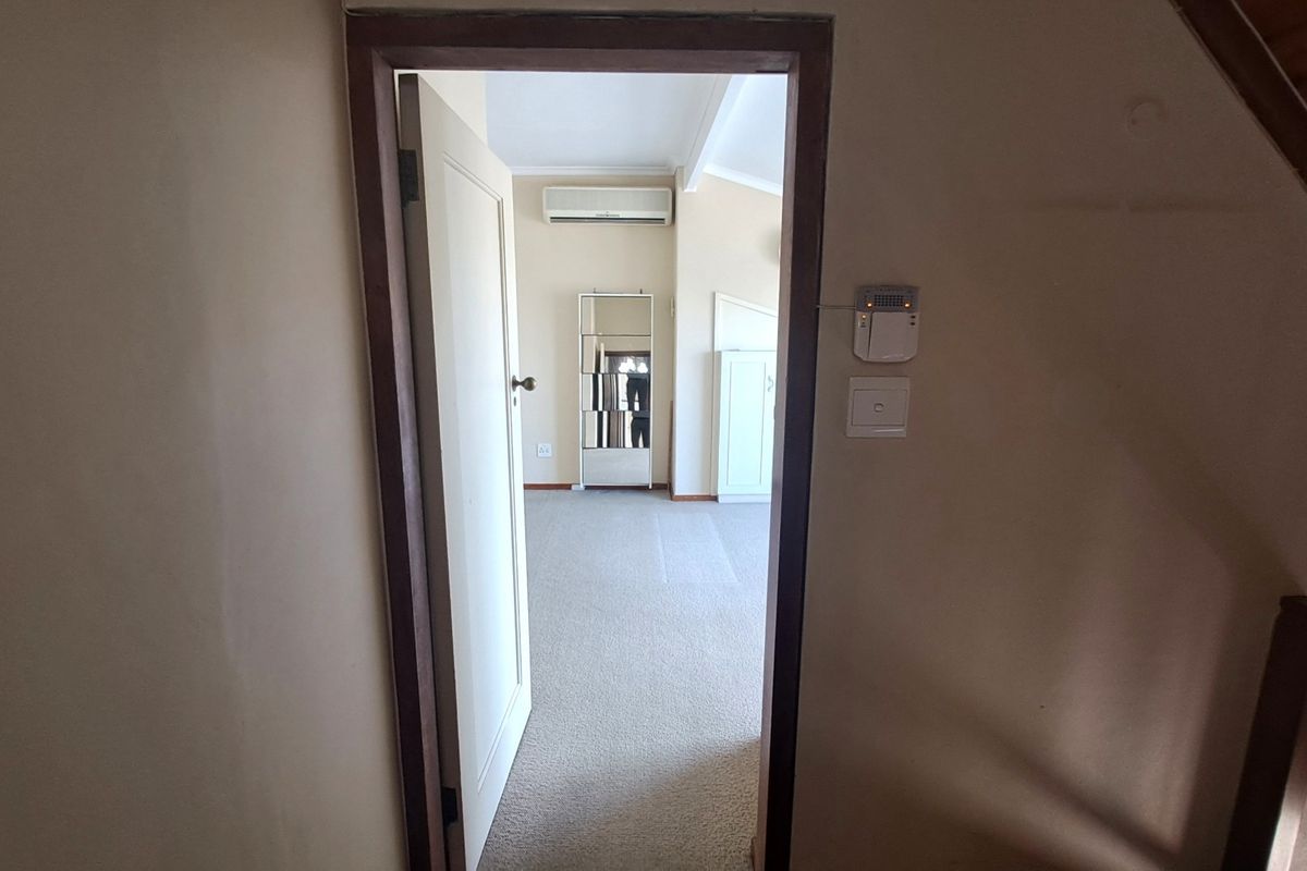 A view through a doorway into an empty bedroom featuring carpeted flooring, built-in cabinetry, and a wall-mounted air conditioning unit.