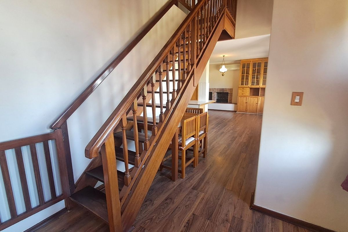 Open plan living area featuring a prominent wooden staircase, laminate flooring, and a fireplace with built-in cabinetry in the background.