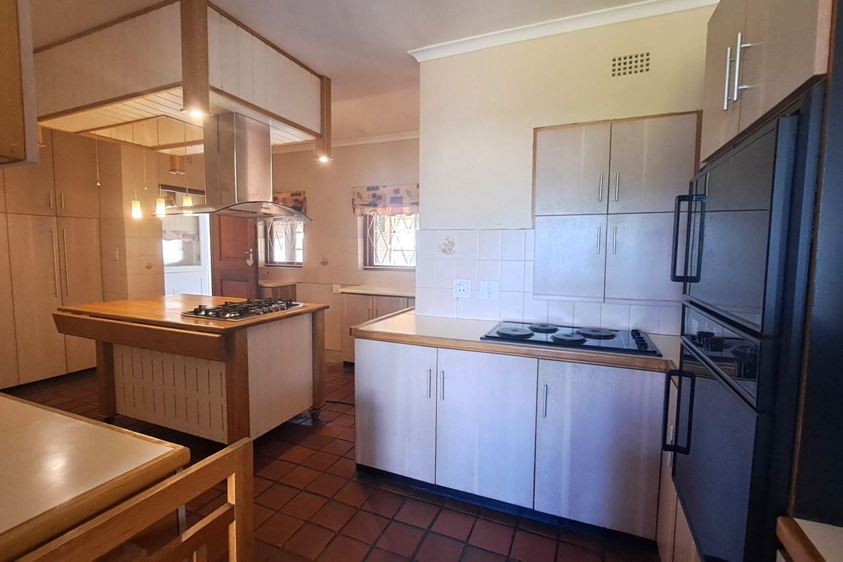 Spacious kitchen featuring a central island with a built-in hob, extractor fan, integrated oven, and ample cabinetry with tiled flooring and backsplash.