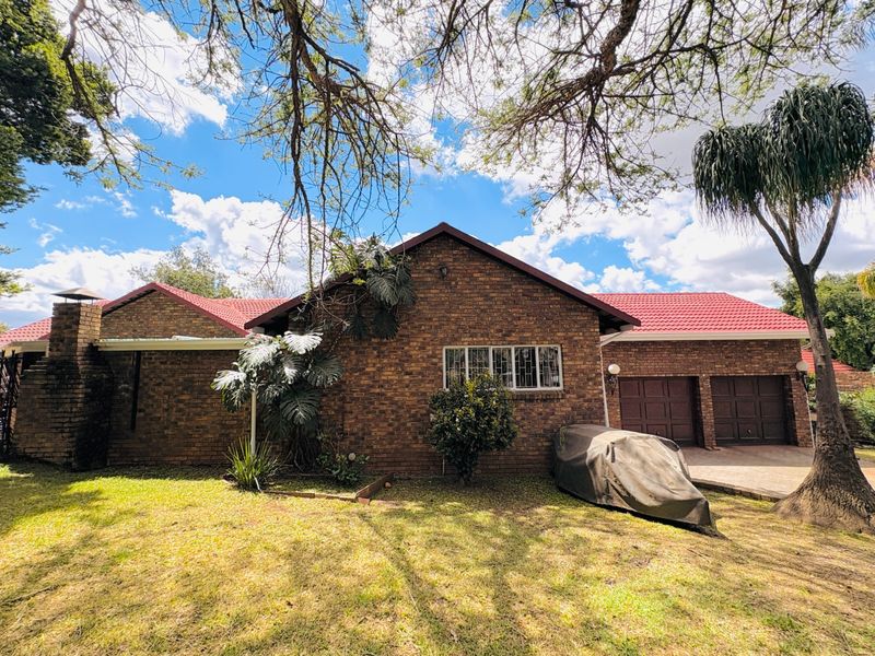 Rear view of a face brick house featuring a tiled roof, external chimney, and a double garage with a paved driveway.