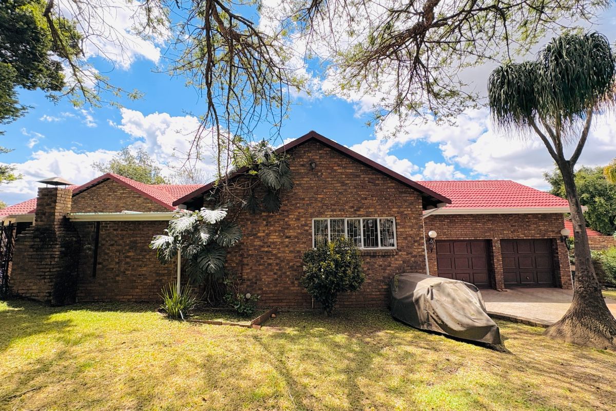 Rear view of a face brick house featuring a tiled roof, external chimney, and a double garage with a paved driveway.