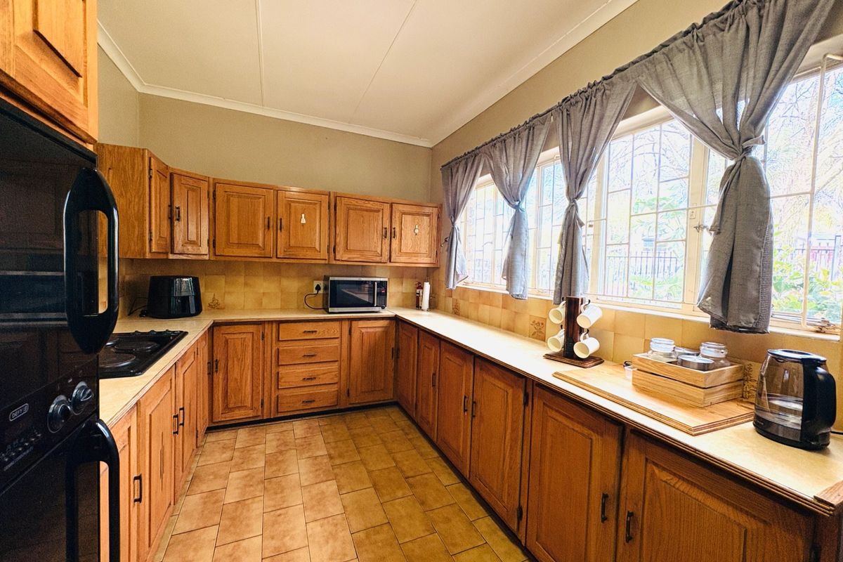 A functional kitchen featuring extensive wooden cabinetry, built-in oven, hob, tiled backsplash, and tiled flooring with large windows providing natural light.