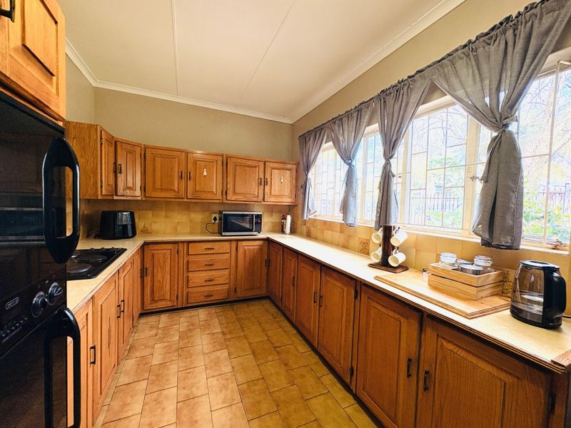 A functional kitchen featuring extensive wooden cabinetry, built-in oven, hob, tiled backsplash, and tiled flooring with large windows providing natural light.