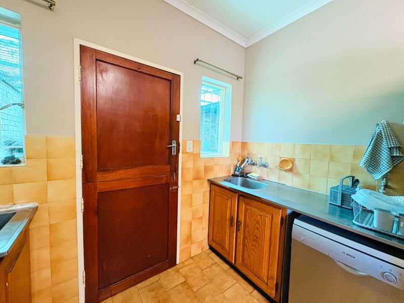 Functional laundry area featuring a stainless steel sink, wooden cabinetry, and tiled splashbacks, providing practical utility space with direct exterior access.