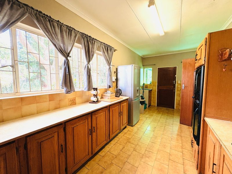 A functional kitchen featuring wooden cabinetry, tiled flooring, a built-in oven, and large windows with security bars, offering a classic, dated aesthetic.