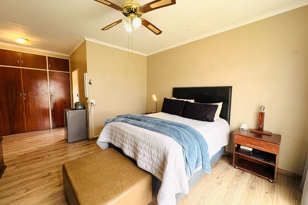 A spacious bedroom featuring laminate flooring, a ceiling fan, and ample built-in cupboard storage.