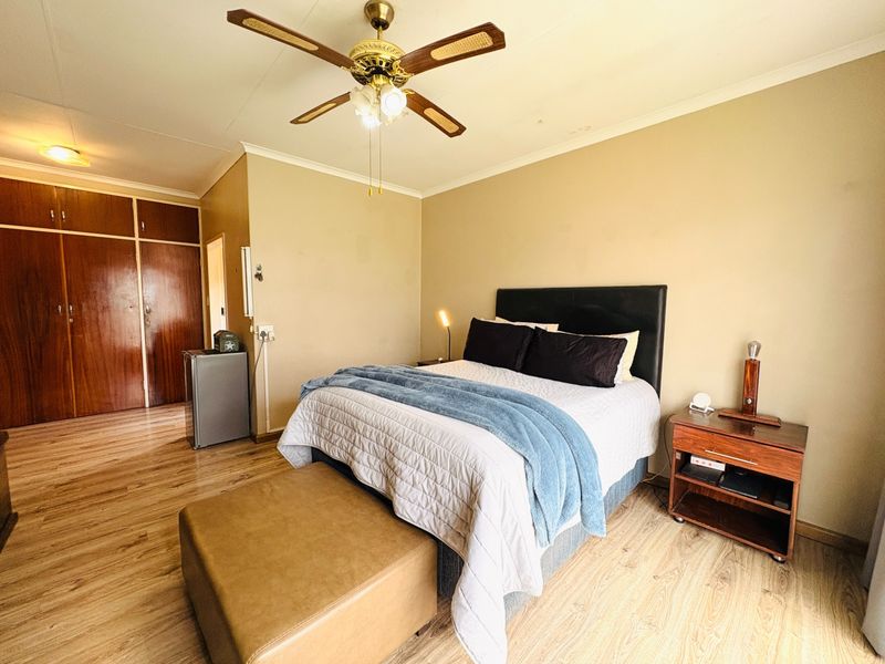 A spacious bedroom featuring laminate flooring, a ceiling fan, and ample built-in cupboard storage.