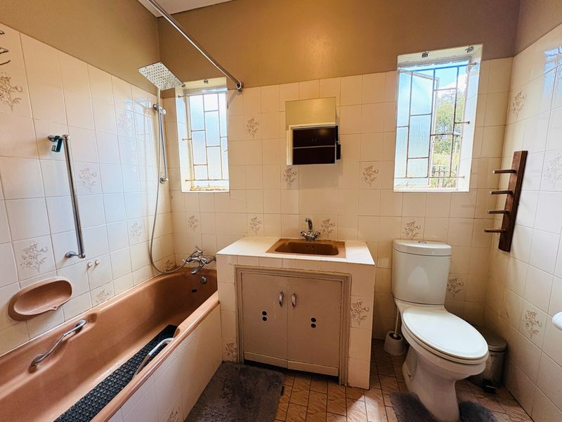 A dated bathroom featuring a built-in vanity, integrated sink, bathtub with shower attachment, and toilet, finished with original wall and floor tiling.