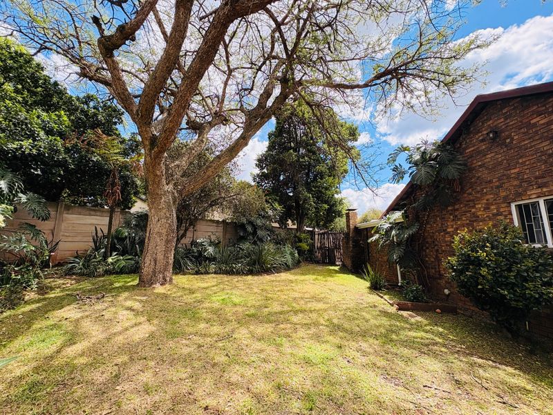 A private rear garden featuring a mature tree, established landscaping, and a brick exterior wall, providing a peaceful outdoor space.