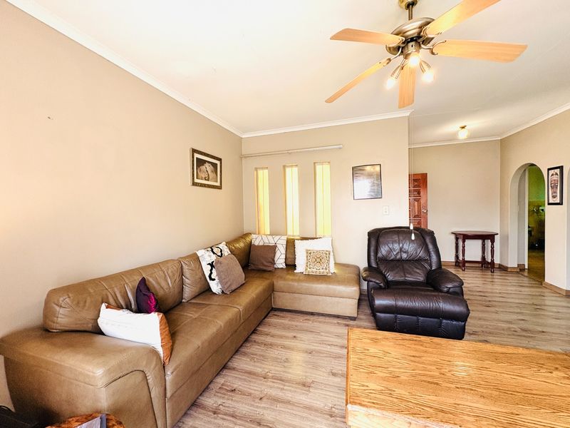 A comfortable living room featuring laminate flooring, a ceiling fan, and unique vertical slit windows, leading through an archway to adjacent living spaces.