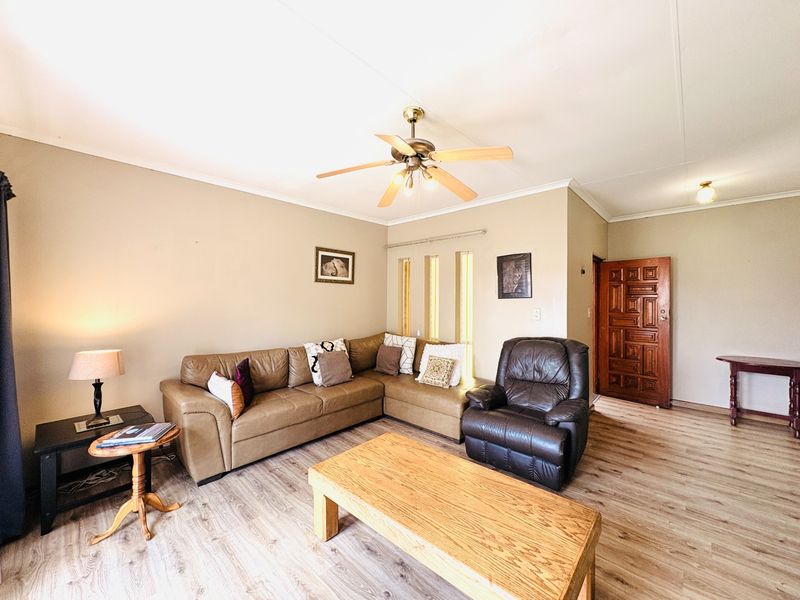 A comfortable living room featuring laminate flooring, a ceiling fan, and a solid wood entrance door with natural light from vertical windows.