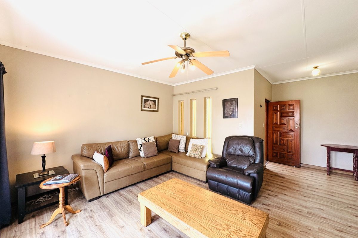 A comfortable living room featuring laminate flooring, a ceiling fan, and a solid wood entrance door with natural light from vertical windows.