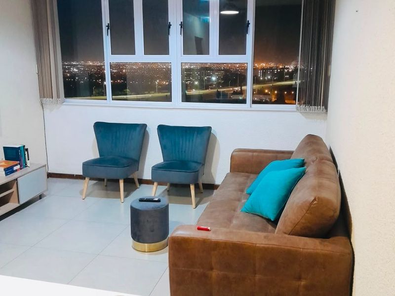 A well-lit living room featuring tiled flooring, a large window with vertical blinds, and a view of the city lights at night.