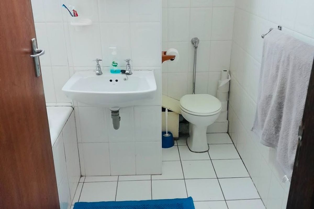 A functional bathroom featuring white ceramic wall and floor tiles, a pedestal washbasin, a toilet, and a bathtub with a wall-mounted medicine cabinet.