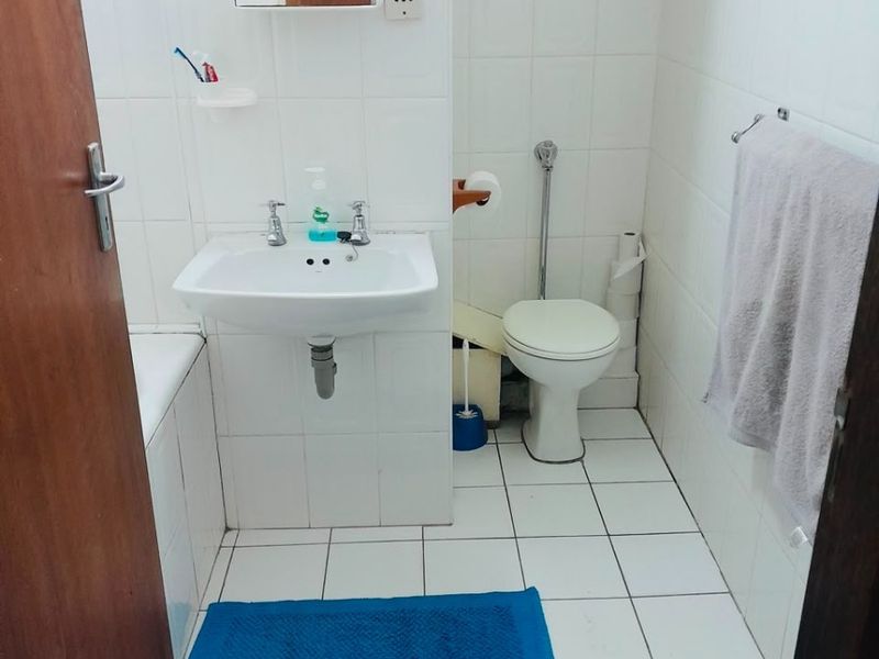A functional bathroom featuring white ceramic wall and floor tiles, a pedestal washbasin, a toilet, and a bathtub with a wall-mounted medicine cabinet.