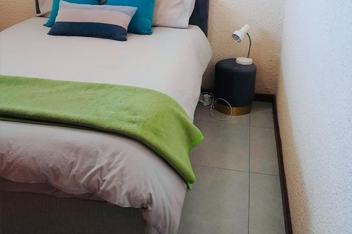 A compact bedroom featuring neutral tiled flooring and textured wall finishes, providing a functional space for rest.