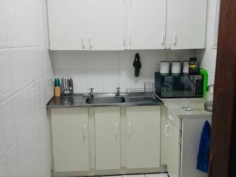 Compact scullery area featuring white built-in cabinetry, stainless steel sink, and fully tiled walls and flooring.
