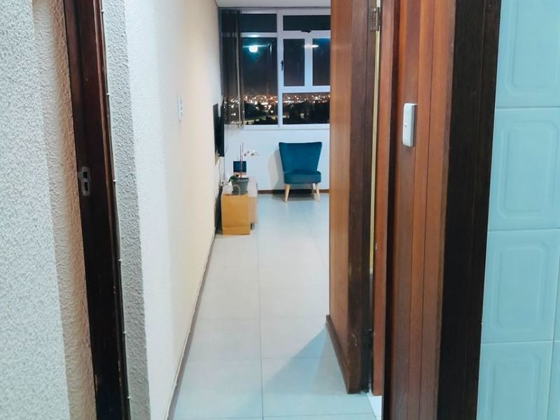 A bright hallway featuring tiled flooring and wooden door frames, leading towards a window with an evening city view.