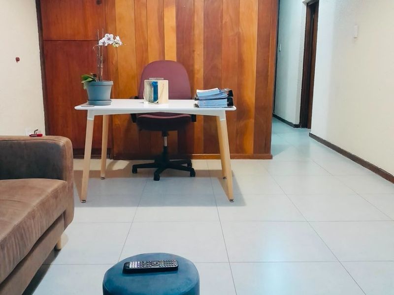 A living area featuring wood paneling accent wall and neutral tiled flooring, providing a versatile space for relaxation or home office use.