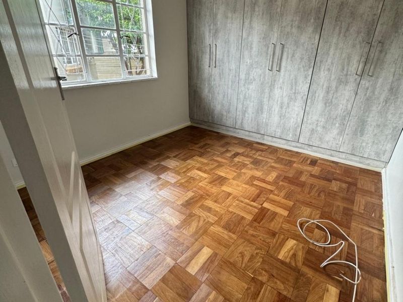 A bright, empty bedroom featuring classic parquet flooring and extensive built-in cupboards with a modern grey finish.