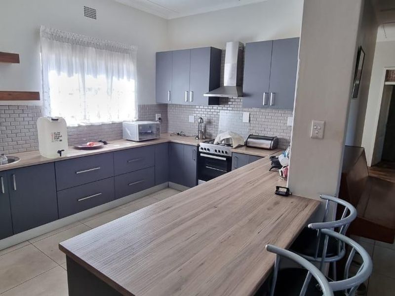 Modern kitchen featuring grey cabinetry, wood-look countertops, subway tile backsplash, and a breakfast bar, offering a functional and contemporary cooking space.