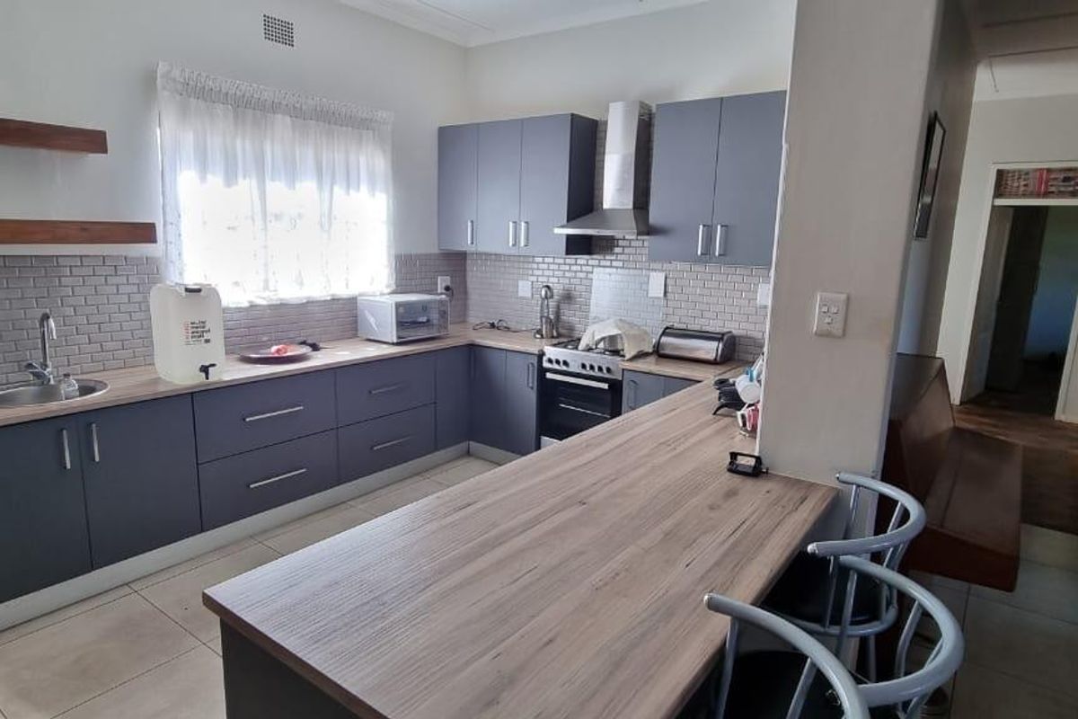 Modern kitchen featuring grey cabinetry, wood-look countertops, subway tile backsplash, and a breakfast bar, offering a functional and contemporary cooking space.