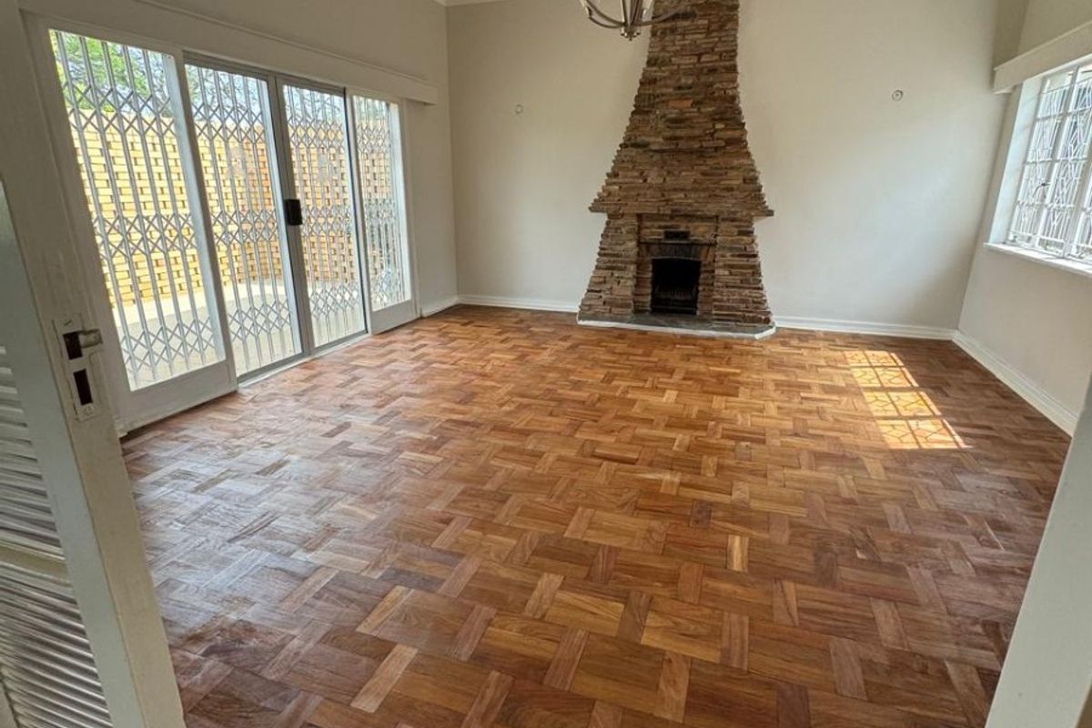Spacious living room featuring beautiful parquet flooring, a prominent stone fireplace, and large sliding glass doors that provide access to the outdoor area.