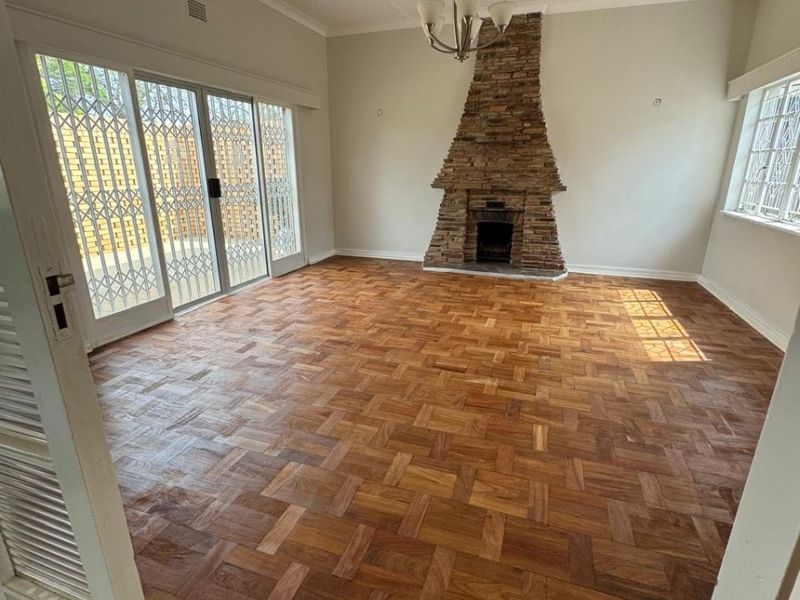 Spacious living room featuring beautiful parquet flooring, a prominent stone fireplace, and large sliding glass doors that provide access to the outdoor area.