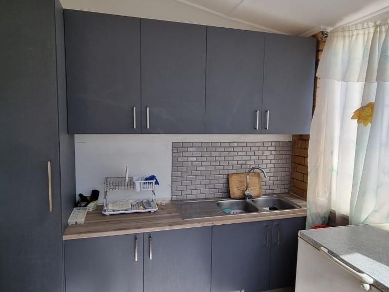 A functional scullery area featuring dark grey cabinetry, a stainless steel double sink, and a subway tile backsplash.