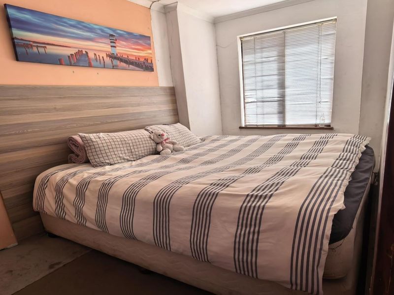 A bedroom featuring a built-in laminate headboard and venetian blinds, showing signs of wear including peeling wall paint and damaged door trim.