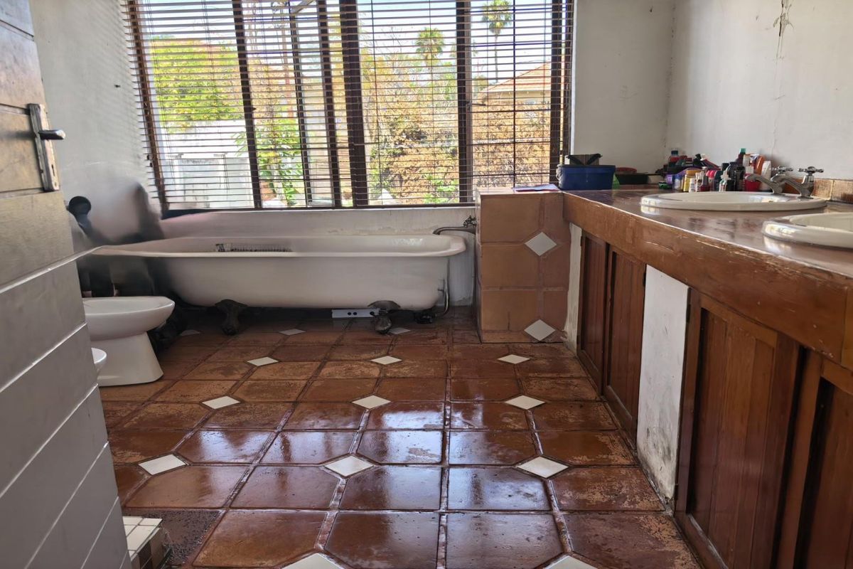 A dated bathroom featuring a classic clawfoot bathtub, double vanity with wooden cabinetry, and traditional tiled flooring.