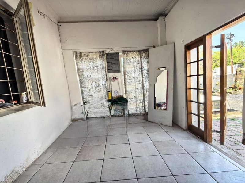 An empty living area featuring tiled flooring, large windows with security bars, and a timber-framed glass door leading to the exterior.