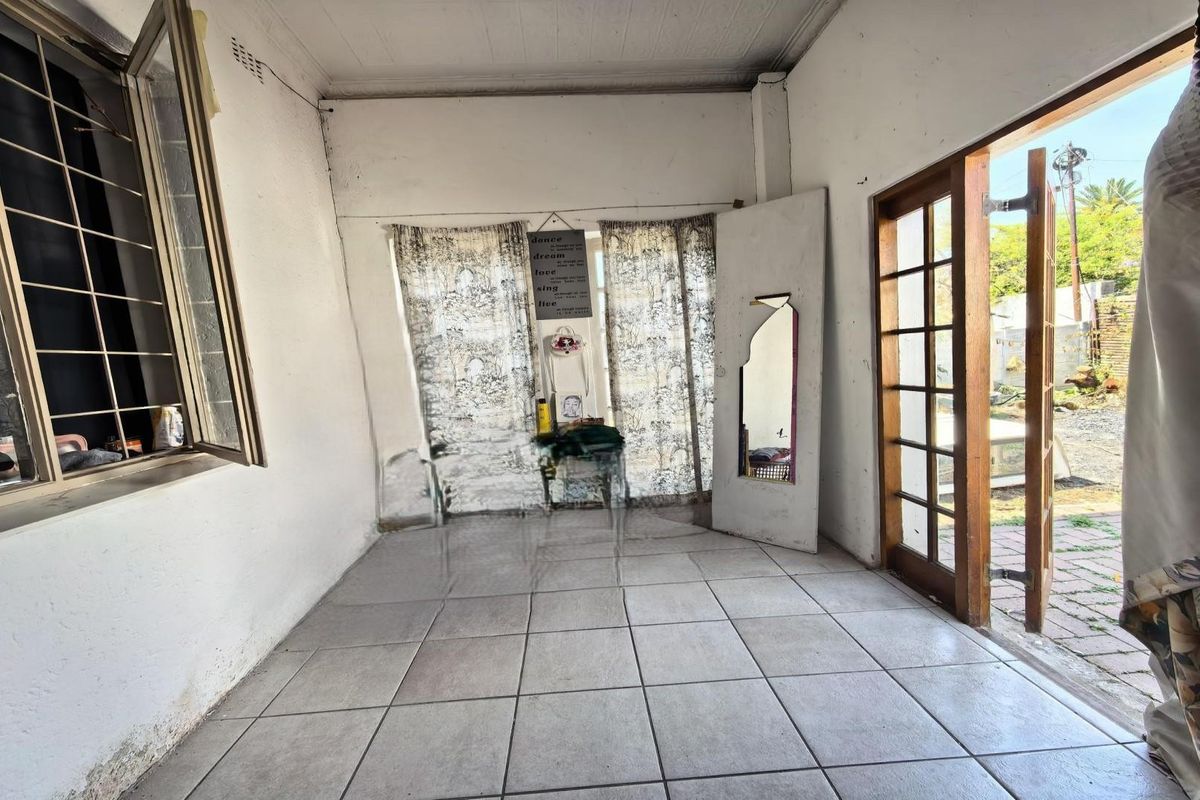 An empty living area featuring tiled flooring, large windows with security bars, and a timber-framed glass door leading to the exterior.