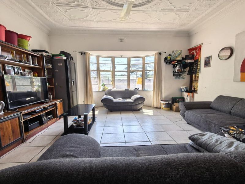 Spacious living room featuring a classic ornate pressed metal ceiling, large bay window, and tiled flooring, offering a solid foundation for modern updates.