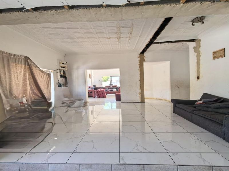 Open-plan living area featuring large marble-look floor tiles and decorative ceiling panels, currently requiring significant finishing and repair work to walls and ceilings.