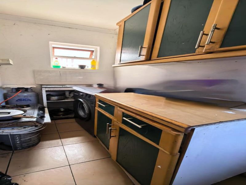 A compact scullery area featuring built-in cabinetry, tiled flooring, and a gas stove setup, requiring cosmetic updates to improve the overall finish.