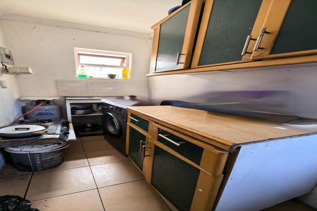 A compact scullery area featuring built-in cabinetry, tiled flooring, and a gas stove setup, requiring cosmetic updates to improve the overall finish.