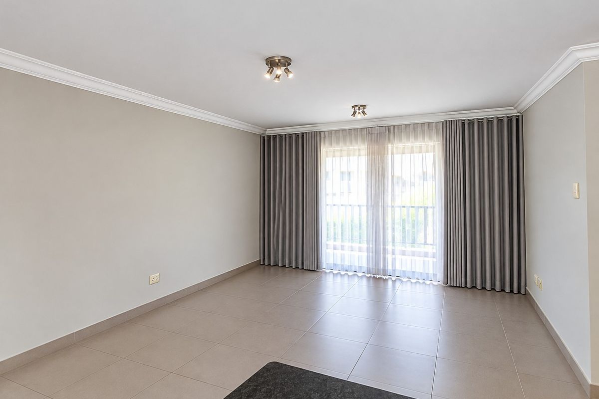 A bright, empty living room featuring neutral tiled flooring, ceiling coving, and large sliding glass doors leading to an outdoor area.