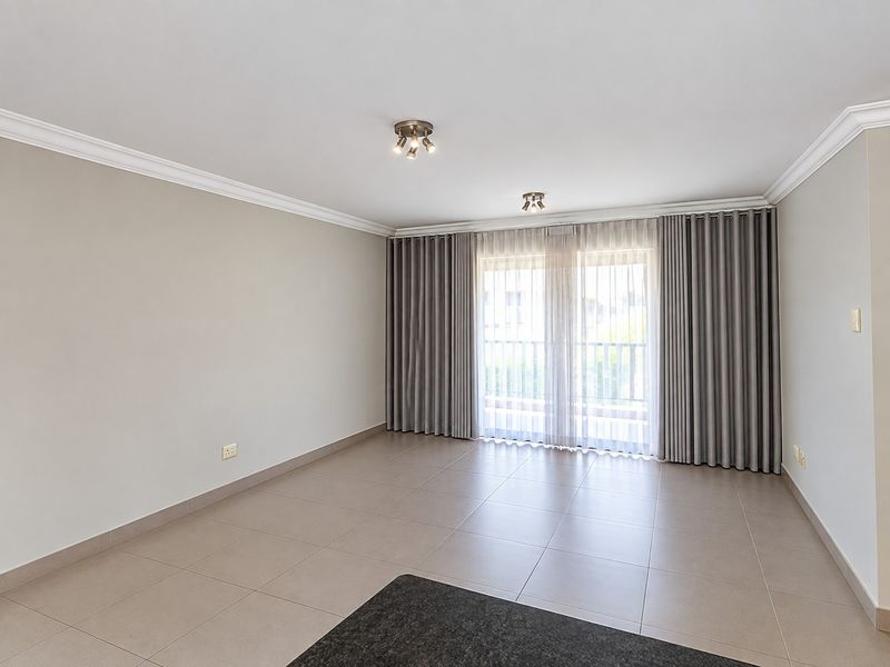 A bright, empty living room featuring neutral tiled flooring, ceiling coving, and large sliding glass doors leading to an outdoor area.