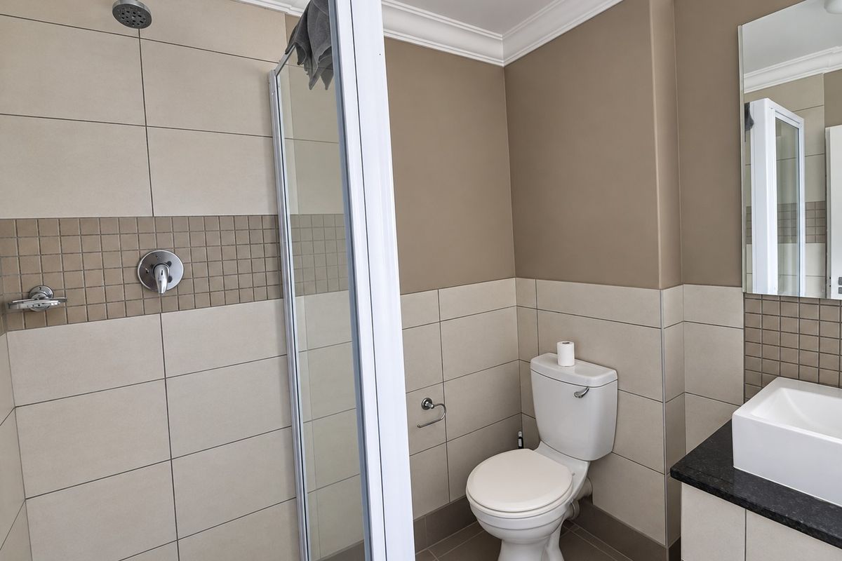 A clean, modern bathroom featuring a glass-enclosed shower, a vanity basin with a granite countertop, and neutral-toned wall tiles.
