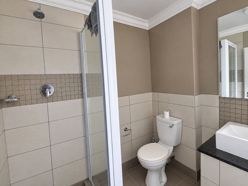 A clean, modern bathroom featuring a glass-enclosed shower, a vanity basin with a granite countertop, and neutral-toned wall tiles.