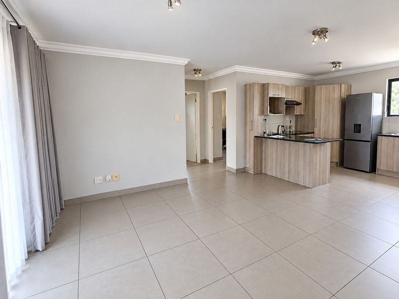 Spacious open-plan living area featuring neutral tiled flooring, modern wood-finish kitchen cabinetry with granite countertops, and recessed ceiling lighting.