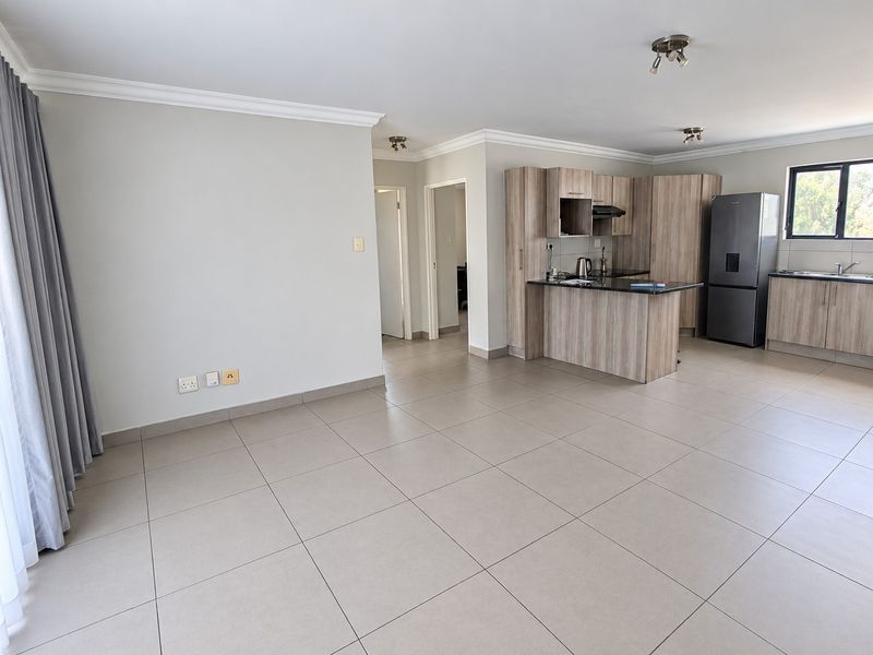 Spacious open-plan living area featuring a modern kitchen with wood-finish cabinetry, granite countertops, and neutral tiled flooring throughout.