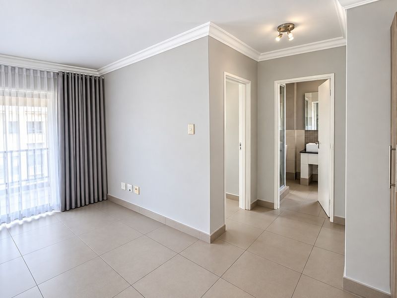 A bright, empty bedroom featuring neutral tiled flooring, modern ceiling cornices, and direct access to a balcony through sliding glass doors.