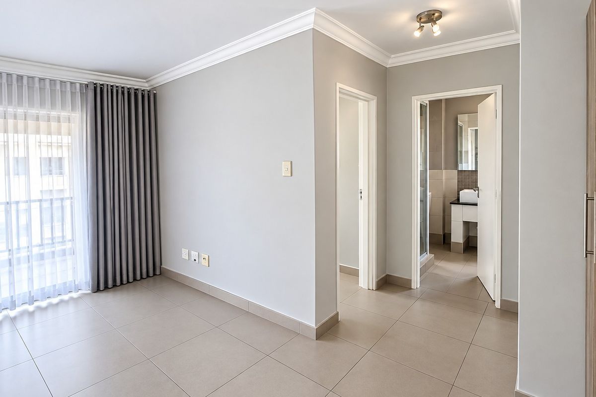 A bright, empty bedroom featuring neutral tiled flooring, modern ceiling cornices, and direct access to a balcony through sliding glass doors.