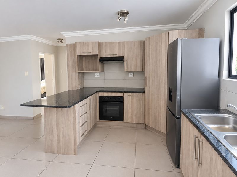Modern kitchen featuring light wood-grain cabinetry, dark granite countertops, built-in oven and hob, and tiled flooring in an open-plan layout.