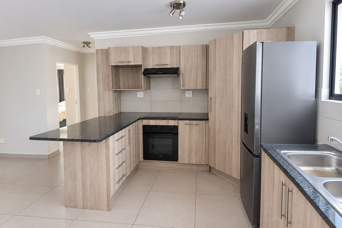 Modern kitchen featuring light wood-grain cabinetry, dark granite countertops, built-in oven and hob, and tiled flooring in an open-plan layout.
