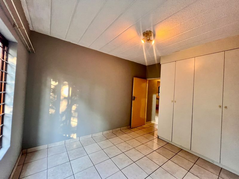 A vacant bedroom featuring tiled flooring, built-in cupboards, and security bars on the window, offering a neutral space ready for personalization.