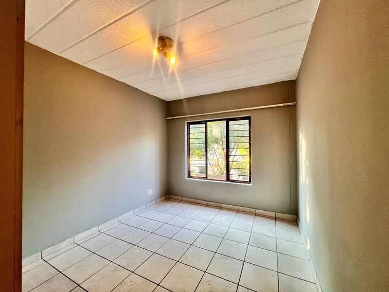 An empty bedroom featuring tiled flooring, a window with security bars, and a textured ceiling, ready for personalization.