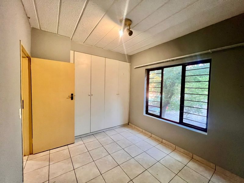 An empty bedroom featuring tiled flooring, built-in cupboards, and a window with security bars, offering a blank canvas for renovation.